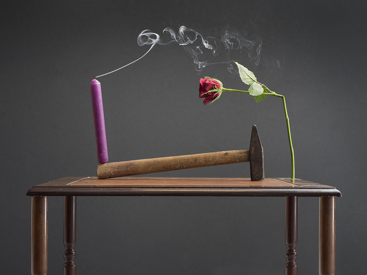 Stilleven met hamer en geknakte roos met uitgedoofte kaars met uitwaaierende rookpluim op antieke tafel